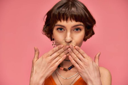 Photo for Cute young woman with nose piercing and short brunette hair sending air kiss on pink background - Royalty Free Image