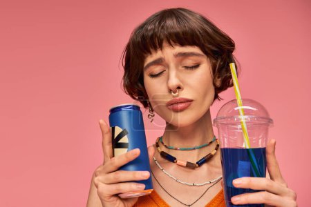 Photo for Young woman with short brunette hair and closed eyes holding blue summer drinks on pink backdrop - Royalty Free Image