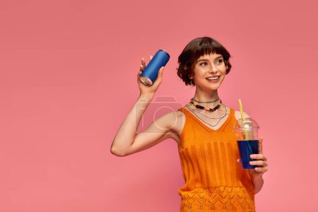 Téléchargez les photos : Heureux jeune femme avec des cheveux bruns courts et piercing tenant boissons d'été sur fond rose - en image libre de droit