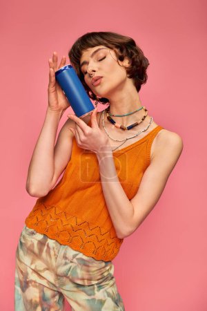 jeune femme aux cheveux bruns courts et aux lèvres boudantes perçant près de la canette de soda sur rose, boisson estivale