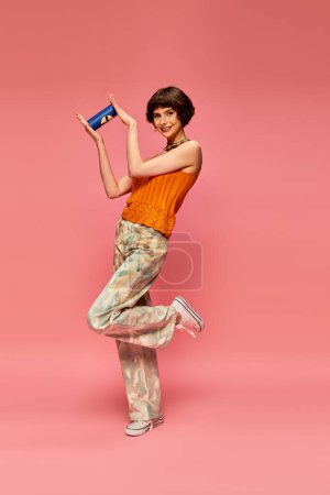 Téléchargez les photos : Contenu jeune femme aux cheveux bruns courts tenant soda peut tout en posant sur rose, boisson d'été - en image libre de droit
