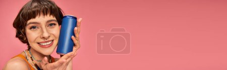 Téléchargez les photos : Bannière de jeune femme joyeuse avec des cheveux bruns courts tenant la canette de soda sur rose, boisson d'été - en image libre de droit
