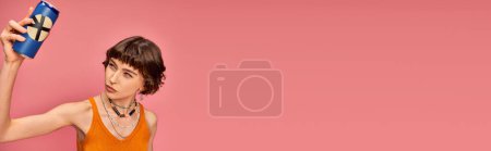 Foto de Dudosa mujer joven con pelo corto morena mirando lata de refresco en rosa, bandera de la bebida de verano - Imagen libre de derechos