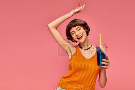 Photo for Excited young woman with short brunette hair holding refreshing summer drink over head on pink - Royalty Free Image