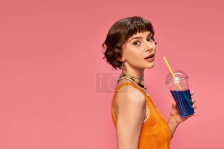 Photo for Pretty young woman with short brunette hair holding refreshing summer cocktail with straw on pink - Royalty Free Image
