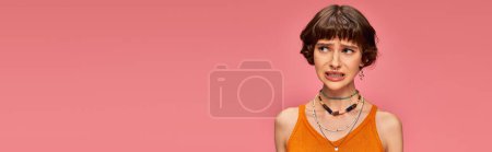 Photo for Puzzled young woman in her 20s standing in orange knitted tank top on pink background, banner - Royalty Free Image