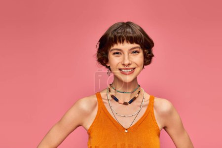 Photo for Cheerful young woman in her 20s with short hair in vibrant tank top smiling on pink background - Royalty Free Image