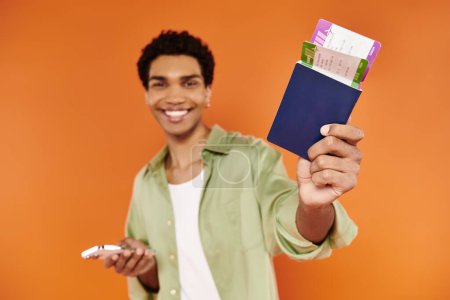 Photo for Good looking jolly african american man holding phone and passport with ticket and smiling at camera - Royalty Free Image