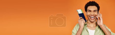 Téléchargez les photos : Joyeux homme afro-américain en tenue confortable parlant par téléphone et tenant un passeport avec billet, bannière - en image libre de droit