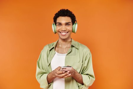 Photo for Joyful trendy african american man with headphones holding his smartphone and smiling at camera - Royalty Free Image
