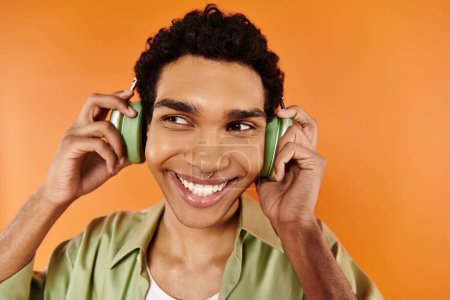 Foto de Hombre afroamericano atractivo feliz en traje acogedor con auriculares mirando hacia otro lado, fondo naranja - Imagen libre de derechos