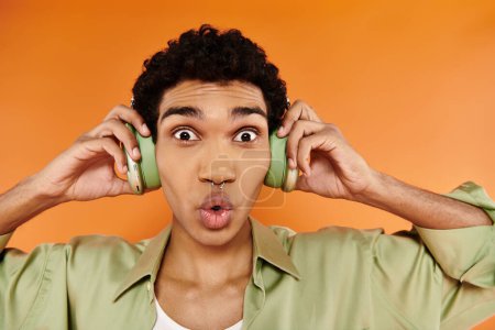Téléchargez les photos : Surpris homme afro-américain attrayant en tenue tendance avec écouteurs et souriant à la caméra - en image libre de droit