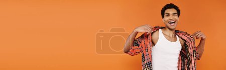 Photo for Jolly african american man in vivid clothing posing on orange backdrop and looking at camera, banner - Royalty Free Image