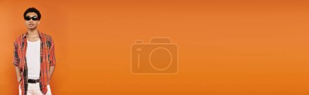 Téléchargez les photos : Jeune homme afro-américain à la mode en tenue vive avec des lunettes de soleil sur fond orange, bannière - en image libre de droit