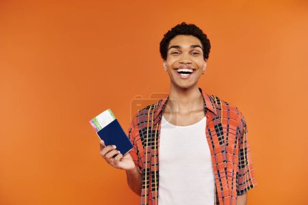 Téléchargez les photos : Joyeux homme afro-américain branché en tenue vive avec passeport et billet et souriant à la caméra - en image libre de droit