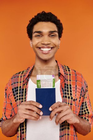 Téléchargez les photos : Homme afro-américain gai en tenue élégante tenant passeport avec billet et souriant à la caméra - en image libre de droit