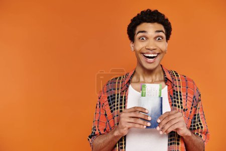 Téléchargez les photos : Joyeux homme afro-américain en tenue élégante tenant passeport avec billet et souriant à la caméra - en image libre de droit