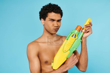 Photo for Good looking young african american man posing with water gun and looking at camera on blue backdrop - Royalty Free Image