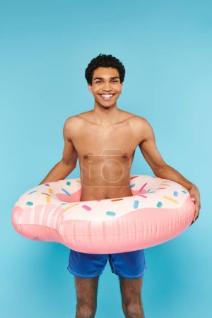 Téléchargez les photos : Beau Africain américain joyeux avec anneau de natation sur fond bleu regardant la caméra - en image libre de droit