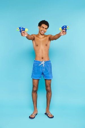 Photo for Joyful handsome african american man posing with two water guns and smiling at camera happily - Royalty Free Image