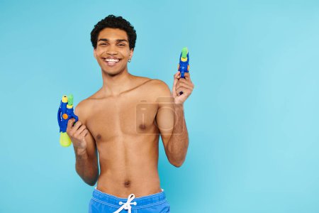 Foto de Alegre guapo afroamericano hombre posando con dos armas de agua y sonriendo a la cámara felizmente - Imagen libre de derechos