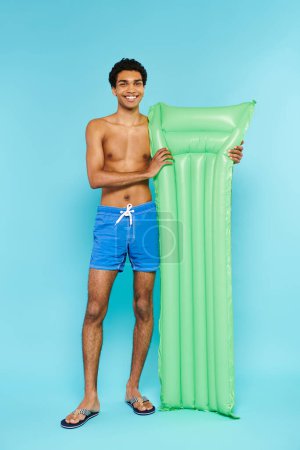 joyful african american man in swimming trunks posing with air mattress and smiling at camera