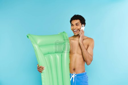 cheerful appealing african american man with air mattress talking by phone and looking away