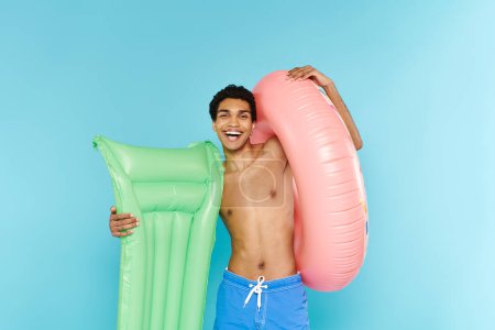joyous african american man posing with air mattress and inflatable donut and smiling at camera