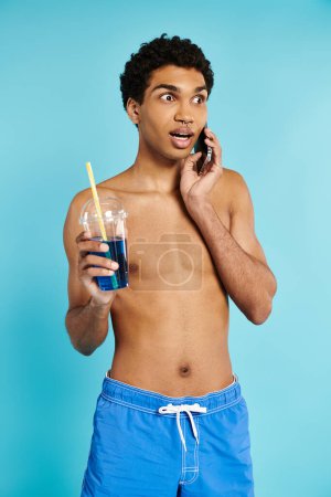 Téléchargez les photos : Bel homme afro-américain parlant par téléphone et tenant un cocktail rafraîchissant dans sa main - en image libre de droit