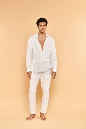 Photo for Alluring young african american man in white attire posing on beige backdrop and looking at camera - Royalty Free Image