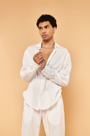 Foto de Guapo chic africano americano hombre en elegante ropa blanca mirando hacia otro lado en beige telón de fondo - Imagen libre de derechos