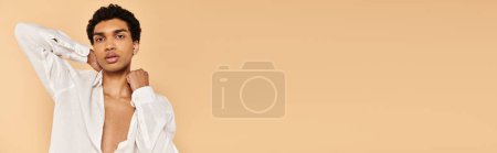 Téléchargez les photos : Chic homme afro-américain en tenue blanche posant sur fond beige et regardant la caméra, bannière - en image libre de droit