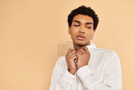 Foto de Atractivo hombre afroamericano elegante en ropa blanca elegante mirando hacia otro lado en fondo beige - Imagen libre de derechos