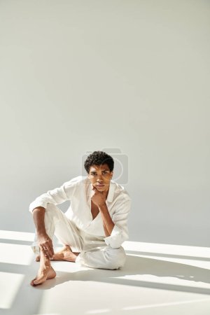 Foto de Pulido joven afroamericano hombre en traje de lino mirando a la cámara en el suelo sobre fondo beige - Imagen libre de derechos