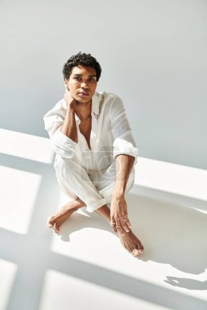 good looking african american man in linen attire looking at camera on floor on beige backdrop