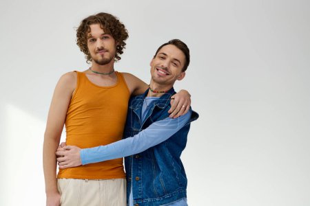 Photo for Positive good looking lgbtq friends in stylish outfits posing on gray backdrop and looking at camera - Royalty Free Image