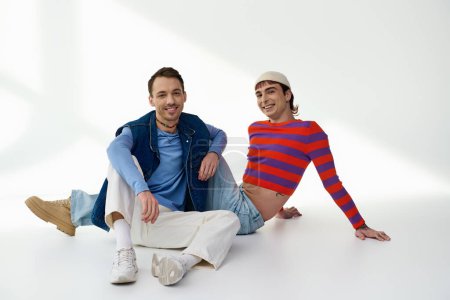 Foto de Dos amigos lgbt de buen aspecto positivo en trajes vibrantes mirando a la cámara posando sobre fondo gris - Imagen libre de derechos