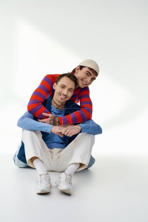 Foto de Dos felices amigos lgbt bien parecido en trajes vibrantes mirando a la cámara posando sobre fondo gris - Imagen libre de derechos