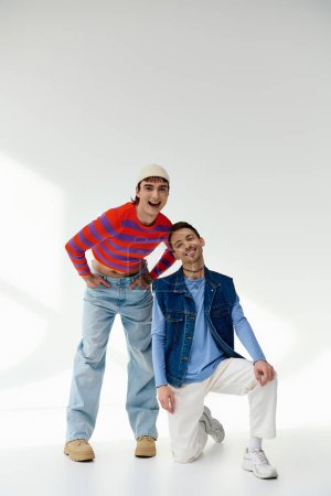 Foto de Dos alegres amigos lgbt bien parecido en trajes vibrantes mirando a la cámara posando sobre fondo gris - Imagen libre de derechos