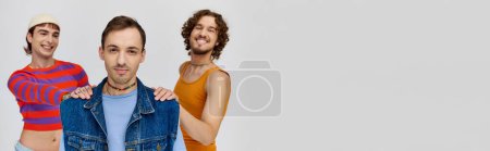 Photo for Happy gay men in vibrant attires posing together on gray backdrop and looking at camera, banner - Royalty Free Image