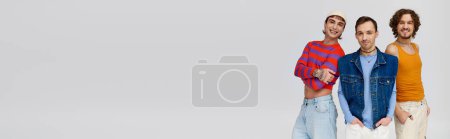 Photo for Jolly gay men in vibrant attires posing together on gray backdrop and looking at camera, banner - Royalty Free Image