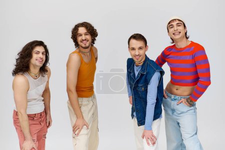 Téléchargez les photos : Quatre gai bien regarder gay les hommes dans vive vêtements souriant à caméra tout en posant sur gris toile de fond - en image libre de droit