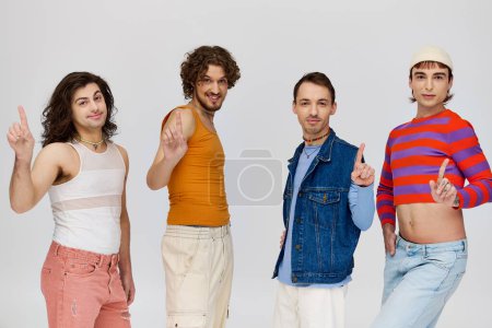 Photo for Four positive good looking gay men in vivid attires smiling at camera while posing on gray backdrop - Royalty Free Image