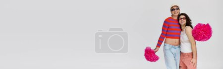 Photo for Cheerful gay men in vibrant attires with sunglasses posing with pom poms on gray backdrop, banner - Royalty Free Image