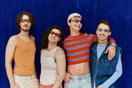 Modisch fröhlich attraktive schwule Männer mit Sonnenbrille in lebendigen Kleidern posieren auf blauem Hintergrund, Stolz