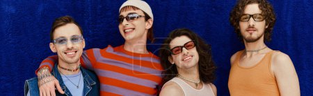 merry handsome gay men with sunglasses in vivid attires posing on blue backdrop, pride month, banner