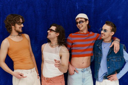 stylische lustige attraktive homosexuelle Männer mit Sonnenbrille in lebendigen Kleidern posieren auf blauem Hintergrund, Stolz