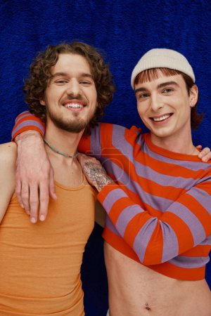 Foto de Dos contento buen aspecto gay los hombres en vibrante ropa posando en oscuro azul telón de fondo, orgullo mes - Imagen libre de derechos