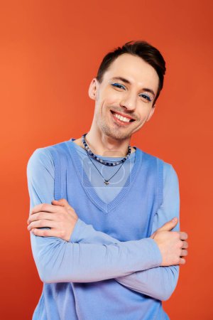 positive attraktive stilvolle Homosexuell Mann mit lebendigen Make-up posiert auf orangefarbenem Hintergrund, Stolz Monat