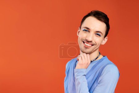 Photo for Cheerful attractive stylish gay man with vibrant makeup posing on orange backdrop, pride month - Royalty Free Image